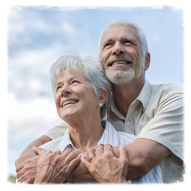 Casal de idosos, com roupas claras, em local ao ar livre, olhando ao longe e sorrindo, numa expressão de satisfação.