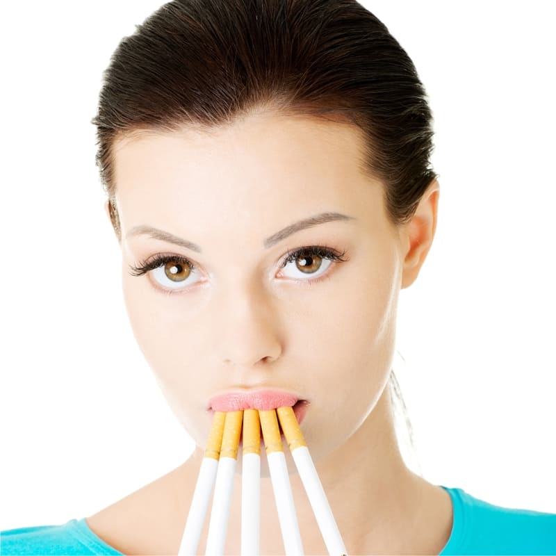 Foto de uma moça de pele clara, cabelos escuros, com uma camiseta verde, e cinco cigarros apagado em sua boca, todos apontados para baixo como se fossem seus dentes, e uma expressão triste, como quem quer livrar-se do vício de fumar.