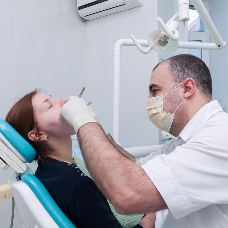 Em um consultório iluminado, um dentista examina a boca de uma paciente.