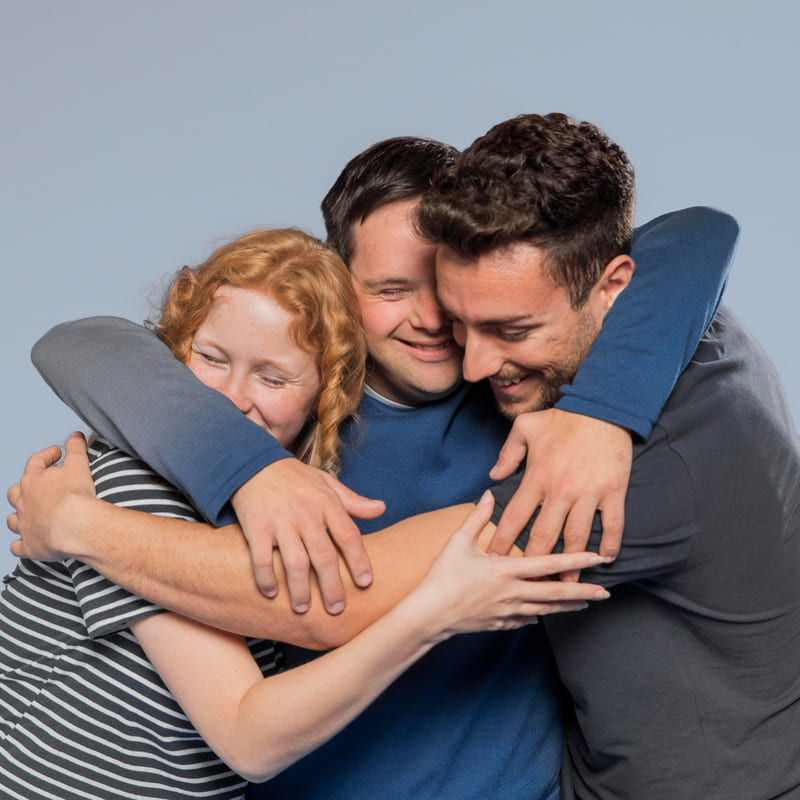 Foto de três jovens se abraçando, dois rapazes e uma moça, todos sorrindo, formando um bom símbolo do dia do abraço.